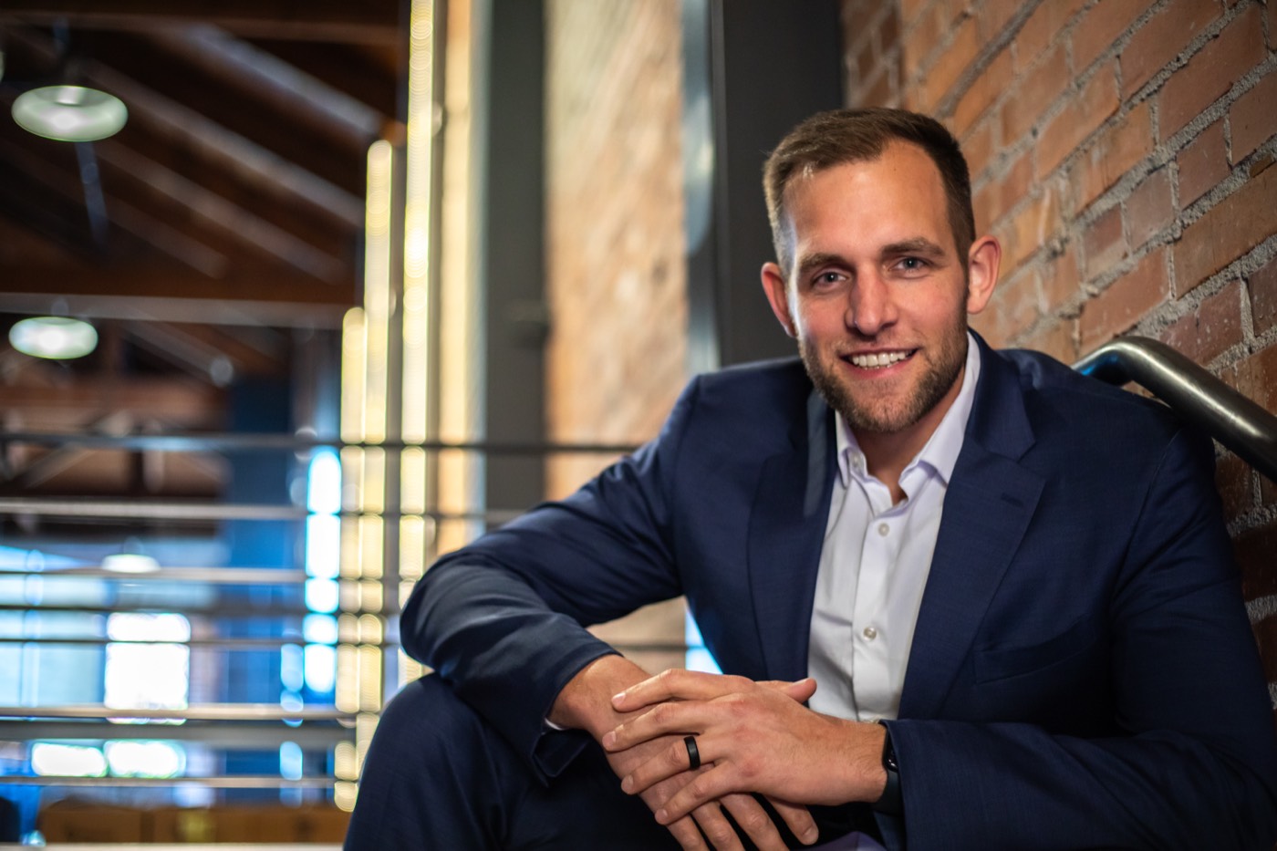 Chris Kiefer in a navy suit, seated in front of a brick wall